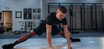 A male athlete stretches intensely in a dimly lit gym environment, preparing for training.